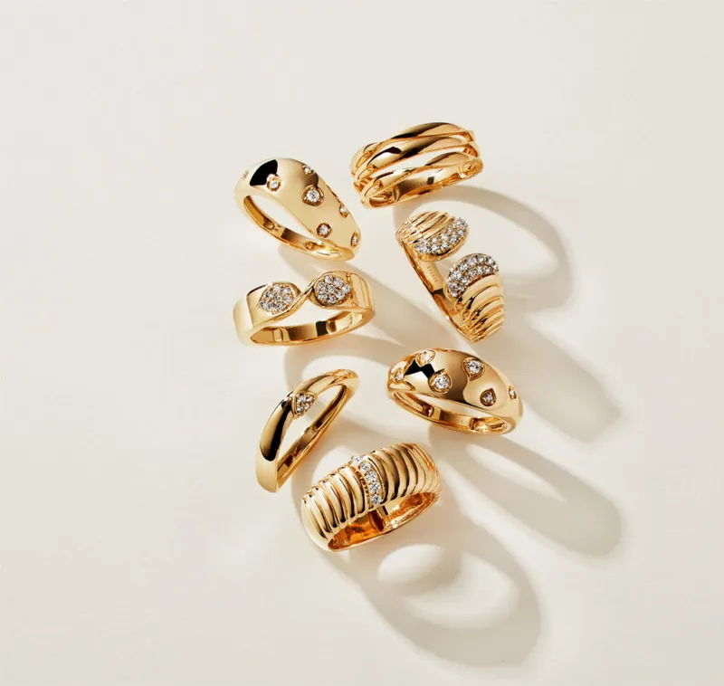 Seven gold rings with diamond accents arranged on a cream surface