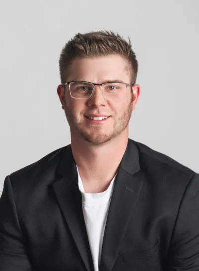Young man with glasses and short hair smiling in a black blazer and white T-shirt
