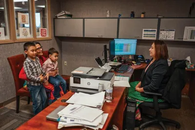 Woman at office desk speaks with a man holding two young children
