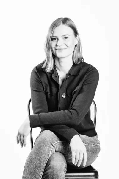 Woman with shoulder-length blonde hair sitting on a chair, smiling, black-and-white portrait