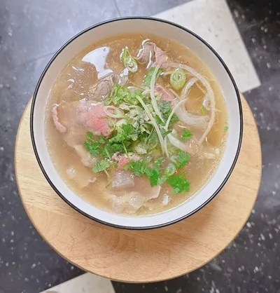 Overhead view of a broth noodle soup topped with fresh herbs, green onions, and sliced meat in a white bowl