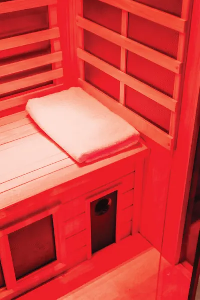 Wooden infrared sauna interior bathed in red light with a folded white towel on the bench