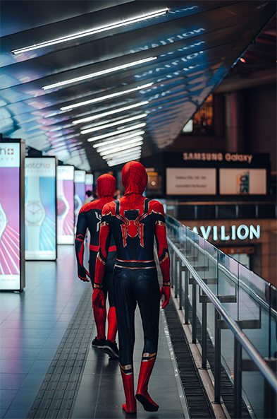 Two people in red and black Spider-Man suits walking through a shopping mall