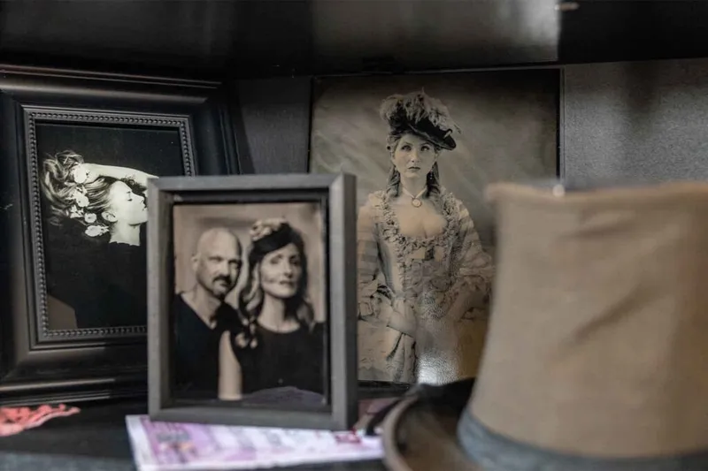 Several dark-framed wet plate portrait photographs displayed on a shelf, including a Victorian-dressed woman and a couple
