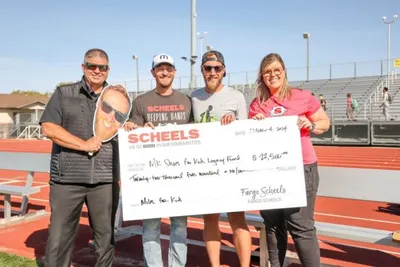 Four people holding a large ceremonial check on a red-track athletic field