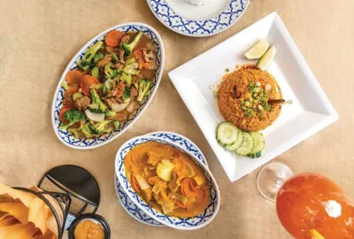 Overhead view of Thai dishes including stir-fried vegetables, curry, and fried rice with cucumber slices