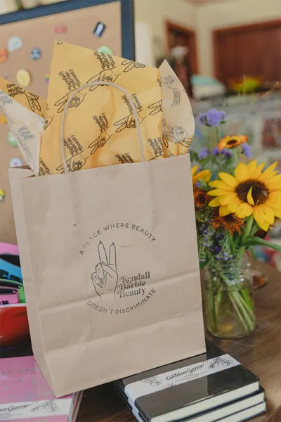 Branded kraft paper gift bag with tissue paper beside a jar of sunflowers on a table