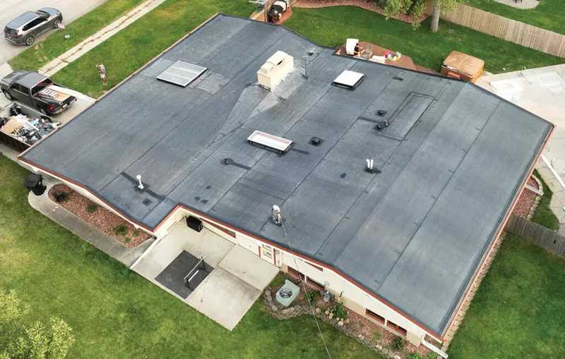 Aerial view of a flat commercial roof with skylights and vents, surrounded by green lawn