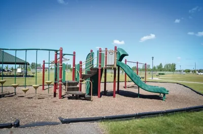 Green and red playground structure with slide on wood chip ground under blue sky