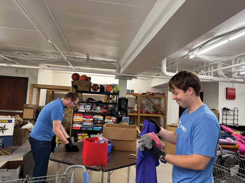Two volunteers in blue shirts sort donated clothing and toys in a warehouse storage room