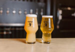 Two hazy golden beers in tulip glasses on a wooden bar