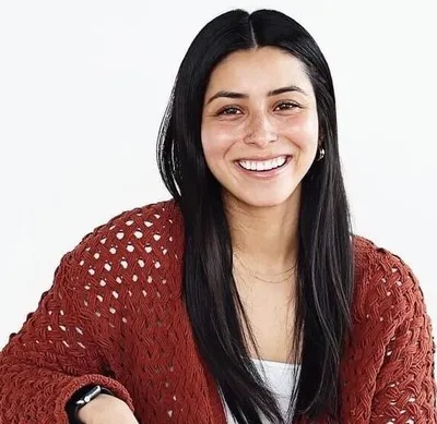 Smiling woman with long black hair wearing a rust-colored open-knit cardigan