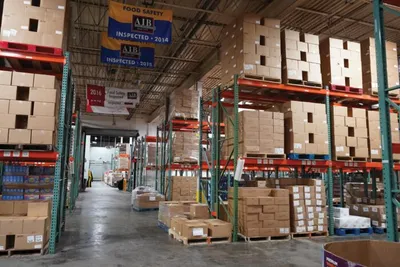Large warehouse with tall green shelving stacked with cardboard boxes and food pallets