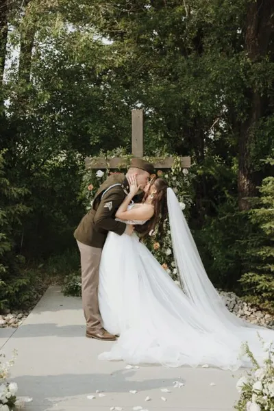 Couple sharing a kiss at an outdoor wedding altar with a wooden cross and lush green trees