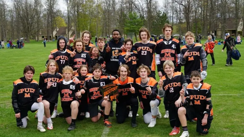 Youth lacrosse team in black and orange Spuds jerseys posing on a grass field