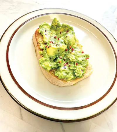 Smashed avocado toast topped with red pepper flakes on a white rimmed plate