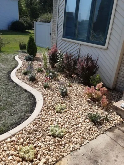 Rock mulch garden bed with shrubs and perennials along a house foundation