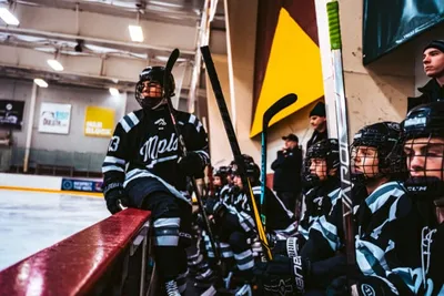 Youth hockey players in matching jerseys on the bench at an indoor rink