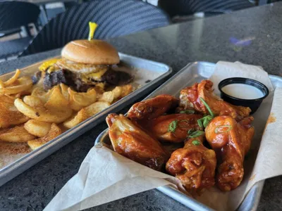 Cheeseburger with fries on a tray beside saucy chicken wings with ranch dipping sauce