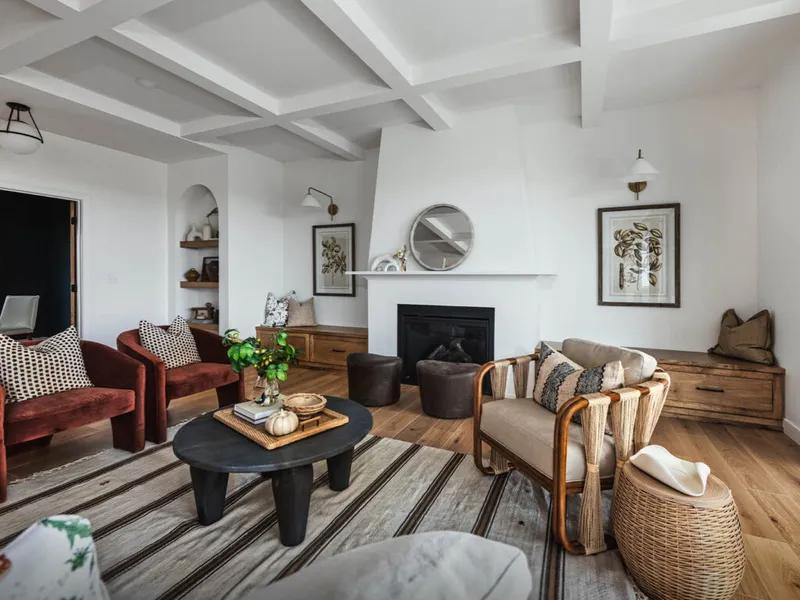Bright living room with coffered ceiling, fireplace, red velvet chairs, and rattan accents on wood floors