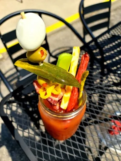 Loaded Bloody Mary in a mason jar topped with pickles, olives, celery, and meat skewer on a metal patio table