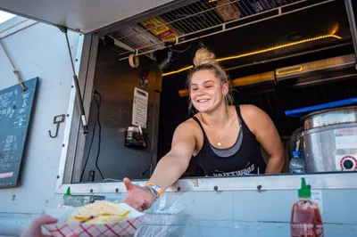 Smiling woman in a food truck window handing a plate of food to a customer