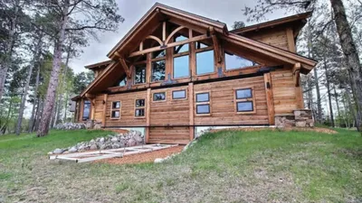 Large log cabin with vaulted wood-framed gable window set among tall pines