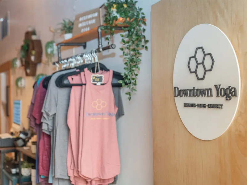 Downtown Yoga branded sign on wood wall beside rack of pink and gray branded tanks and tees