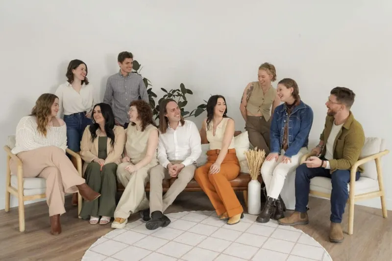 Group of ten smiling people seated and standing together in a bright minimalist studio space