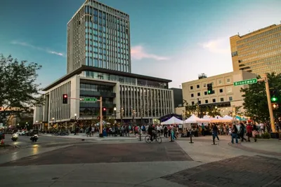 Crowds gathered at an outdoor urban plaza near a tall modern building at dusk