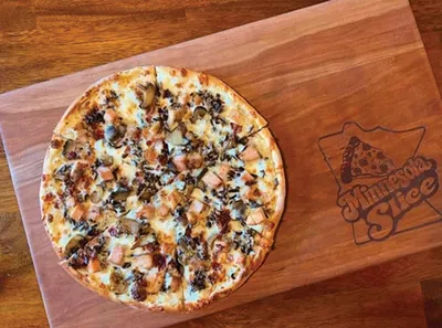 Whole pizza topped with chicken, mushrooms, and herbs on a wooden cutting board