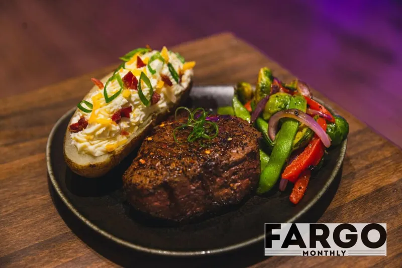 Grilled steak filet with a loaded baked potato and sautéed vegetables on a dark round plate