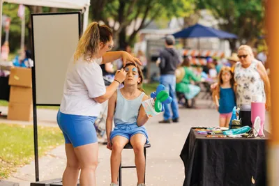 Woman painting a young girl's face at an outdoor community festival