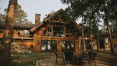 Rustic log cabin lodge with large windows and stone chimney surrounded by trees