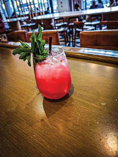 Pink cocktail with fresh mint garnish and black straw on a wooden bar top