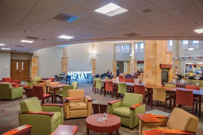 Spacious college lounge with green and red chairs, small tables, and an illuminated M State sign in the background