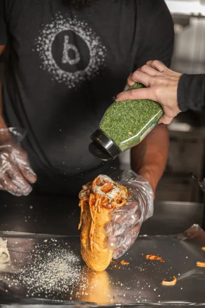Food worker squeezing green sauce onto a filled taco over a metal prep surface