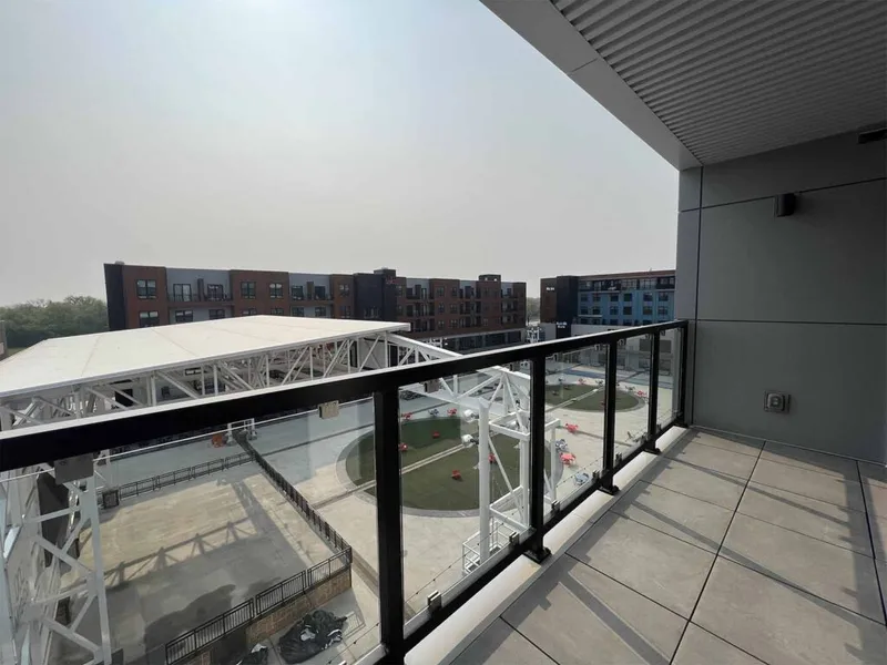 High-rise balcony with glass railing overlooking a mixed-use plaza and brick apartment buildings