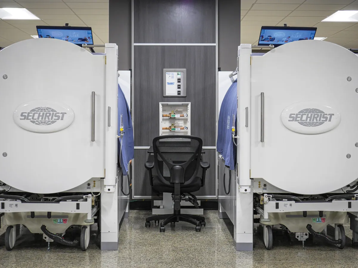 Two Sechrist hyperbaric chambers flanking an empty office chair in a clinical treatment room