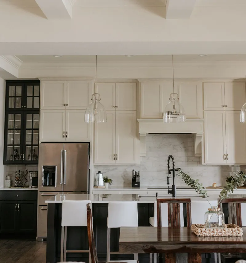 Open-concept kitchen with white cabinetry, marble backsplash, glass pendant lights, and dark island with white stools