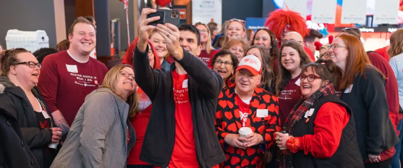 Large group in red shirts smiling for a selfie at an indoor charity event