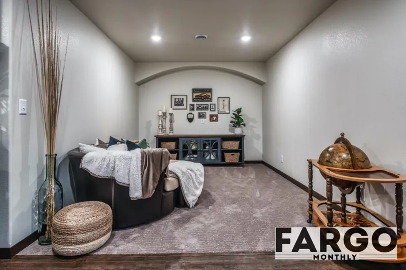 Cozy basement lounge with dark leather sectional, woven pouf, wooden globe stand, and gallery wall beneath an arched ceiling
