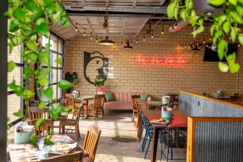 Casual restaurant dining room with brick walls, a neon sign reading 'love me tender,' and a rooster mural