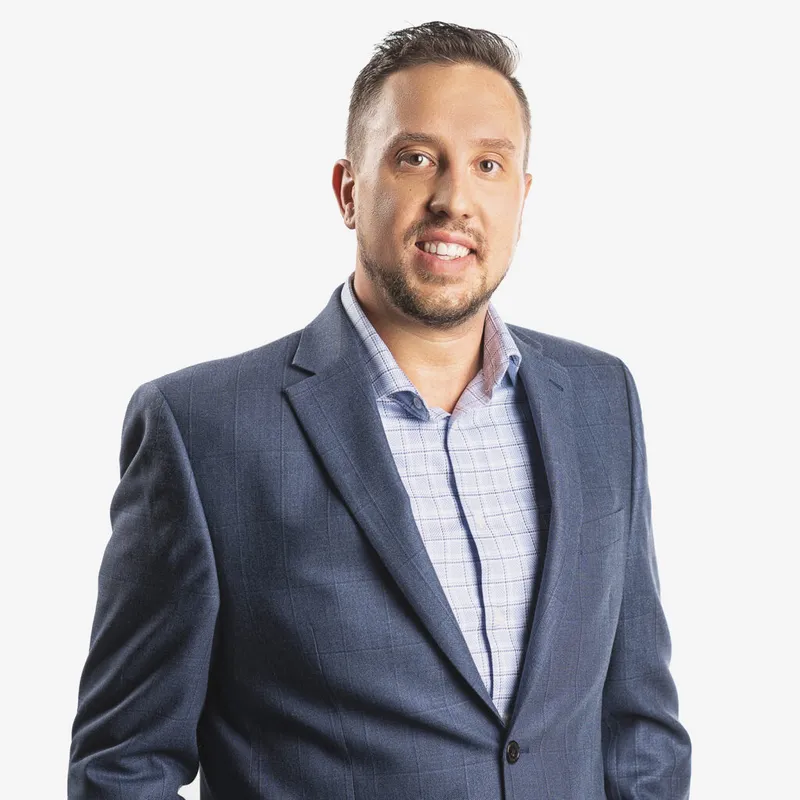 Smiling man with short beard wearing a navy blazer and light plaid shirt