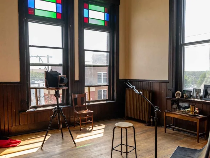 Vintage large-format camera on tripod in a sunlit studio with stained-glass windows and a skull on a side table