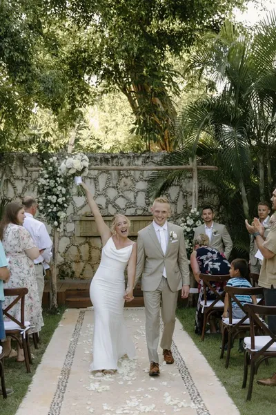 Bride raising bouquet and groom walking back down the aisle at an outdoor garden wedding ceremony