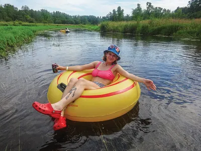 Smiling woman in a pink bikini and bucket hat floating on a yellow inner tube on a calm river