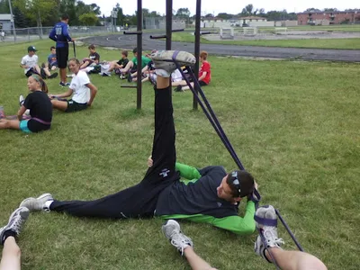 Person doing resistance band exercise on grass while children stretch nearby outdoors