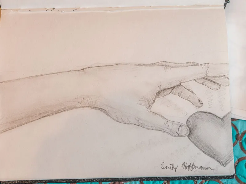 Pencil sketch of an outstretched hand holding a heart, signed in cursive on sketchbook page