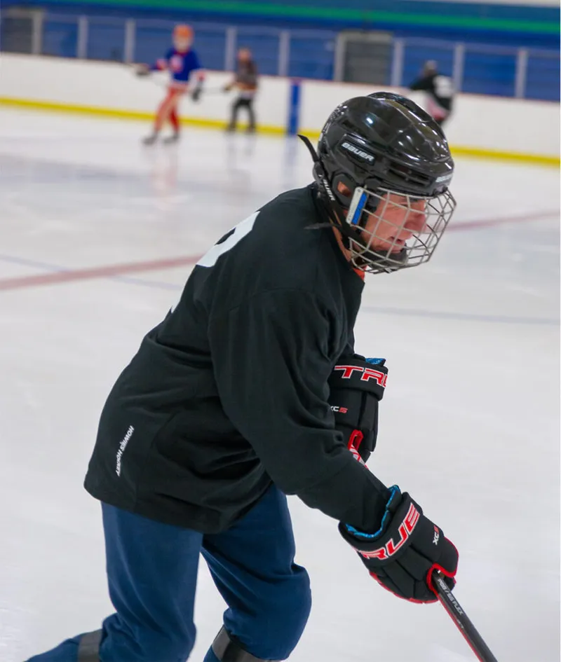 Elderly hockey player in black jersey and Bauer cage helmet skating on indoor rink